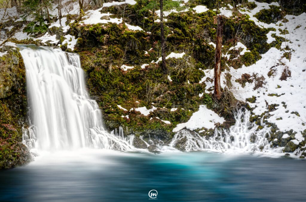 Snowy waterfall flowing into the vibrant turquoise Blue Pool on the McKenzie River in Oregon.