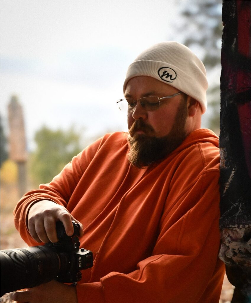 Alexander Malloy adjust a camera lens outdoors wearing an orange hoodie and white beanie.