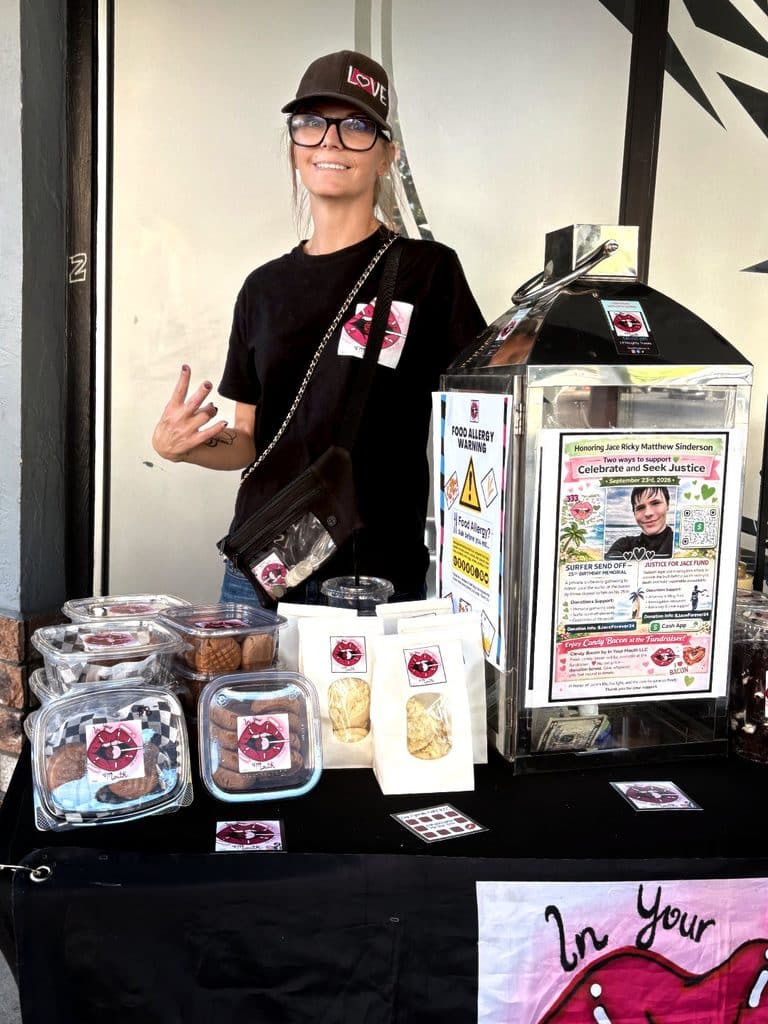 Vegi Hoyt at an In Your Mouth LLC vendor booth with packaged baked goods and a memorial donation display for Jace.