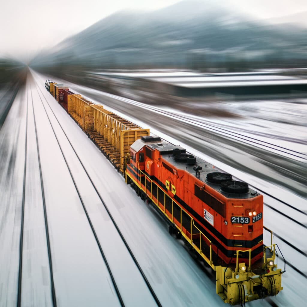 Orange freight train speeding along snow-covered railway tracks toward a mountain in Grants Pass, Oregon.