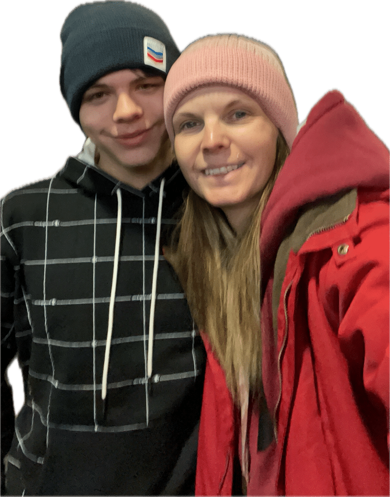 Vegi Hoyt and her son Jace smiling warmly together in winter beanies and jackets against a dark background.